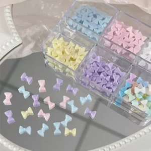 Pastel resin nail bows in six compartments with matching charms scattered on the table