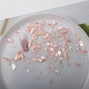 Close-up of pink abalone nail flakes scattered on white dish
