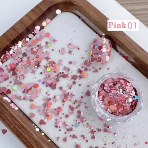 Pink holographic nail sequins with hearts and stars in a glass jar, spilled onto white tray