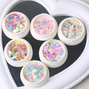 Rainbow pastel nail sequins in white jars with star and alphabet glitter, displayed on a heart-shaped mirror