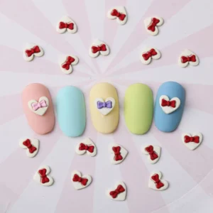 Red bow heart nail charms styled around pastel nail art on pink striped background