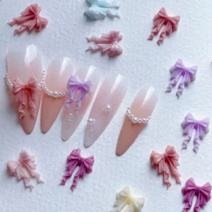 Pastel resin ribbon bow nail decorations displayed on nude and pearl-accented tips