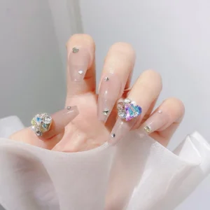 Close-up of luxury rhinestone heart nail charm on nude coffin nails