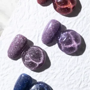 Purple and burgundy glitter nail swatches shown on light surface