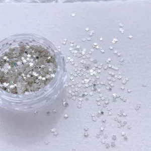 Silver star-shaped nail glitter sequins scattered beside clear container