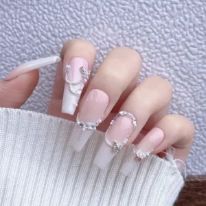 Hand with long white ombré nails adorned with zircon butterfly nail charms and silver chains