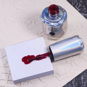 Red gel polish on disposable gel color pad next to bottle