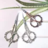 Three ornate vintage nail scissors in silver, gold, and rose gold finishes on floral background